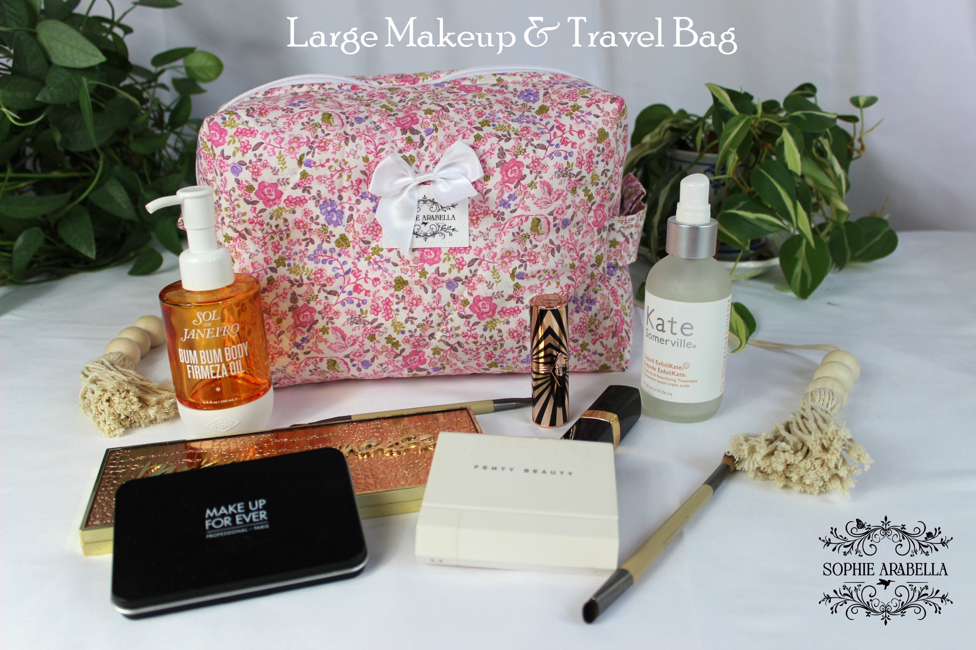 Large makeup and travel bag with cosmetic items on a white surface with greenery.