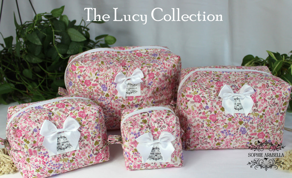 Set of floral makeup bags with white ribbons labeled 'The Lucy Collection' on a neutral background.
