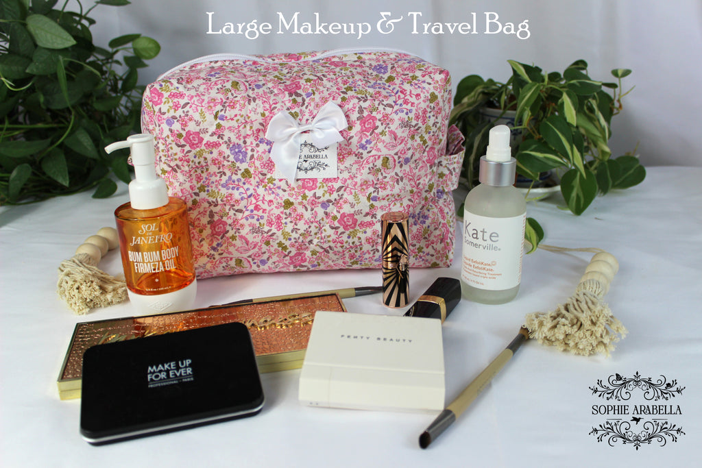 Large makeup and travel bag with cosmetic items on a white surface with greenery.